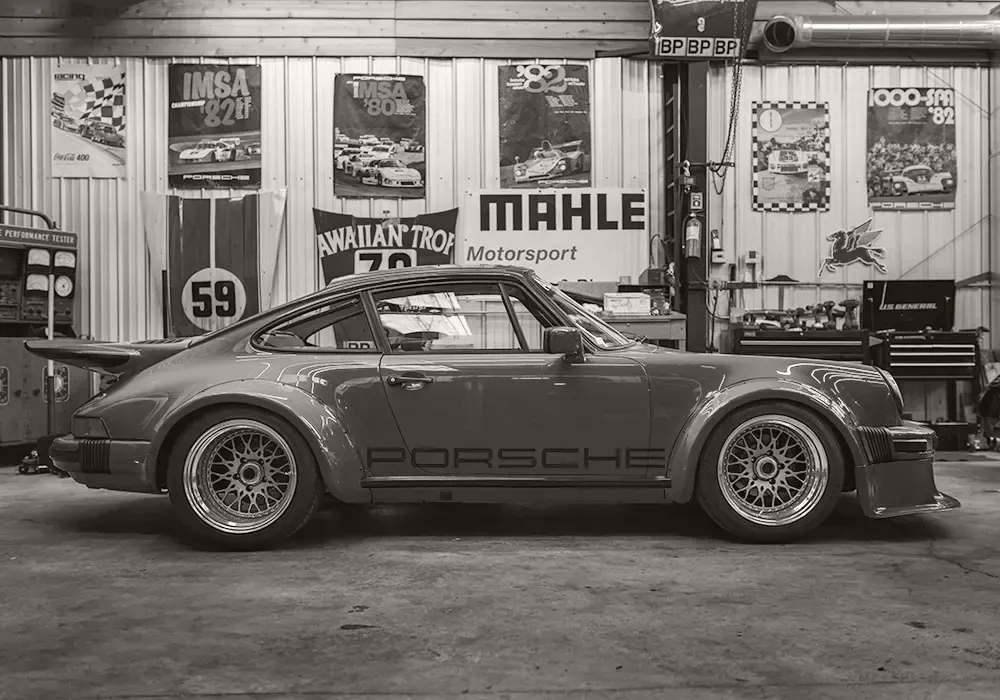 Porsche 911 IMSA-style car inside a motorsport garage, surrounded by racing history and mechanical purpose.