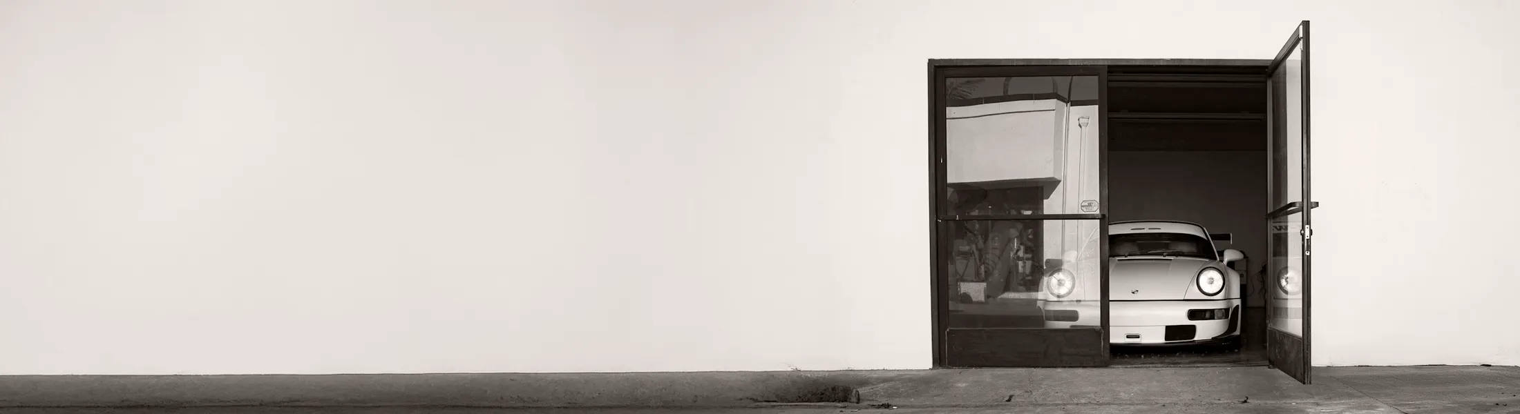 Porsche 911 viewed through glass garage doors, emphasising the quiet boundary between the car’s private space and the outside world.